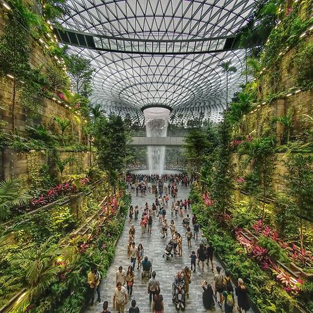 Crowne Plaza Changi Airport By Ihg Singapore Exterior foto The photo depicts a vibrant indoor garden space, characterized by lush greenery and a towering waterfall at its center. The setting features vertical gardens on stone walls, filled with various plants and flowers. People can be seen walking along the