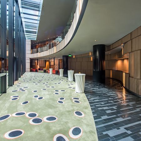 Crowne Plaza Changi Airport By Ihg Singapore Exterior foto The photo shows a modern indoor space that features a curved hallway with a mix of materials and textures. The floor is divided into two sections: one has a smooth, dark tiled design, while the other has a soft, green carpet with circular patterns in