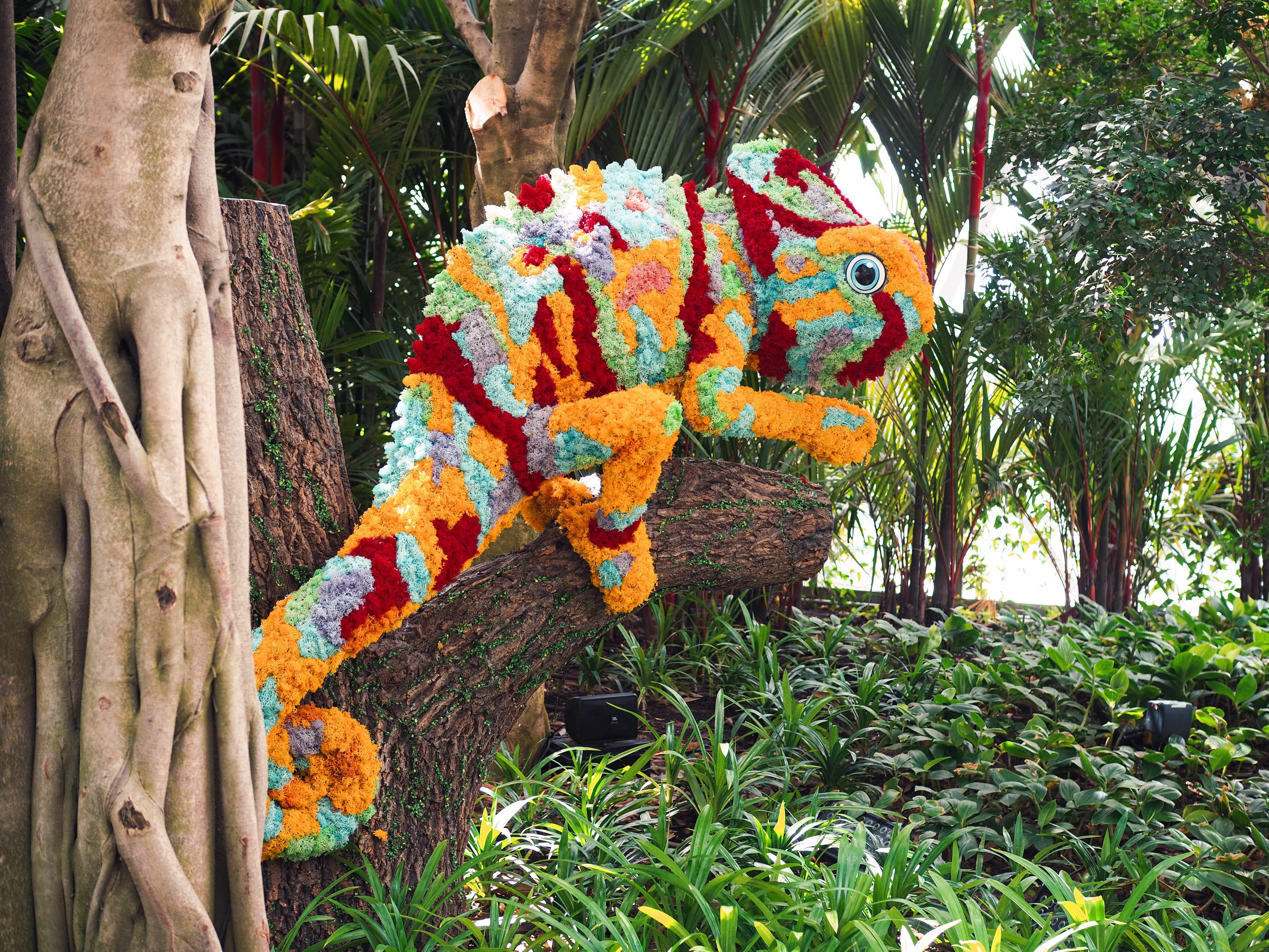 Crowne Plaza Changi Airport By Ihg Singapore Exterior foto The photo shows a vibrant and colorful chameleon sculpture made from flowers and plant materials. The chameleon is positioned on a tree trunk, blending in with the lush greenery of its surroundings. The colors of the sculpture include shades of orang