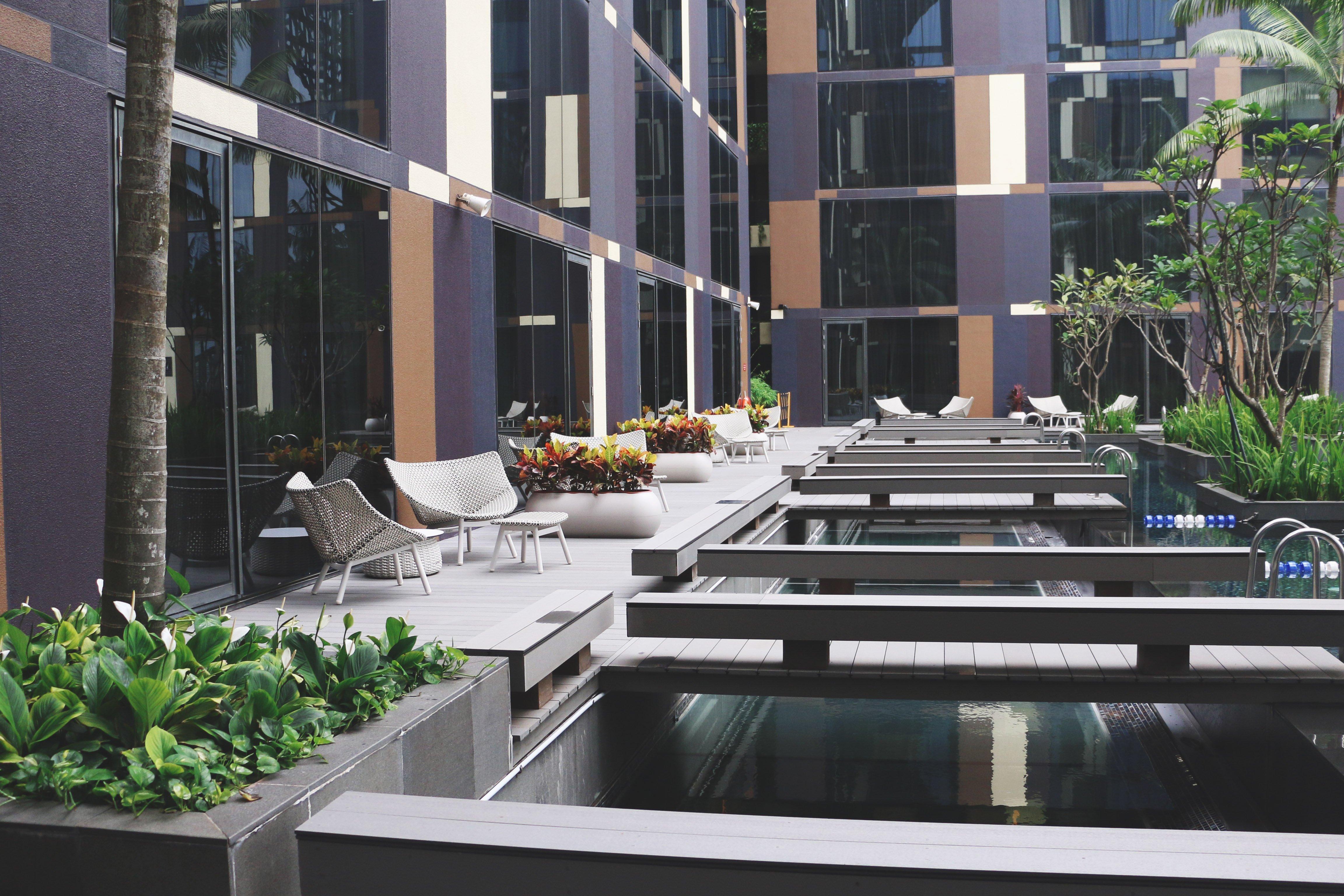 Crowne Plaza Changi Airport By Ihg Singapore Exterior foto The photo shows a modern outdoor area featuring a sleek, contemporary design. There are large glass windows reflecting the surroundings, and the space includes wooden decks over water features. Comfortable seating areas are arranged along the decking