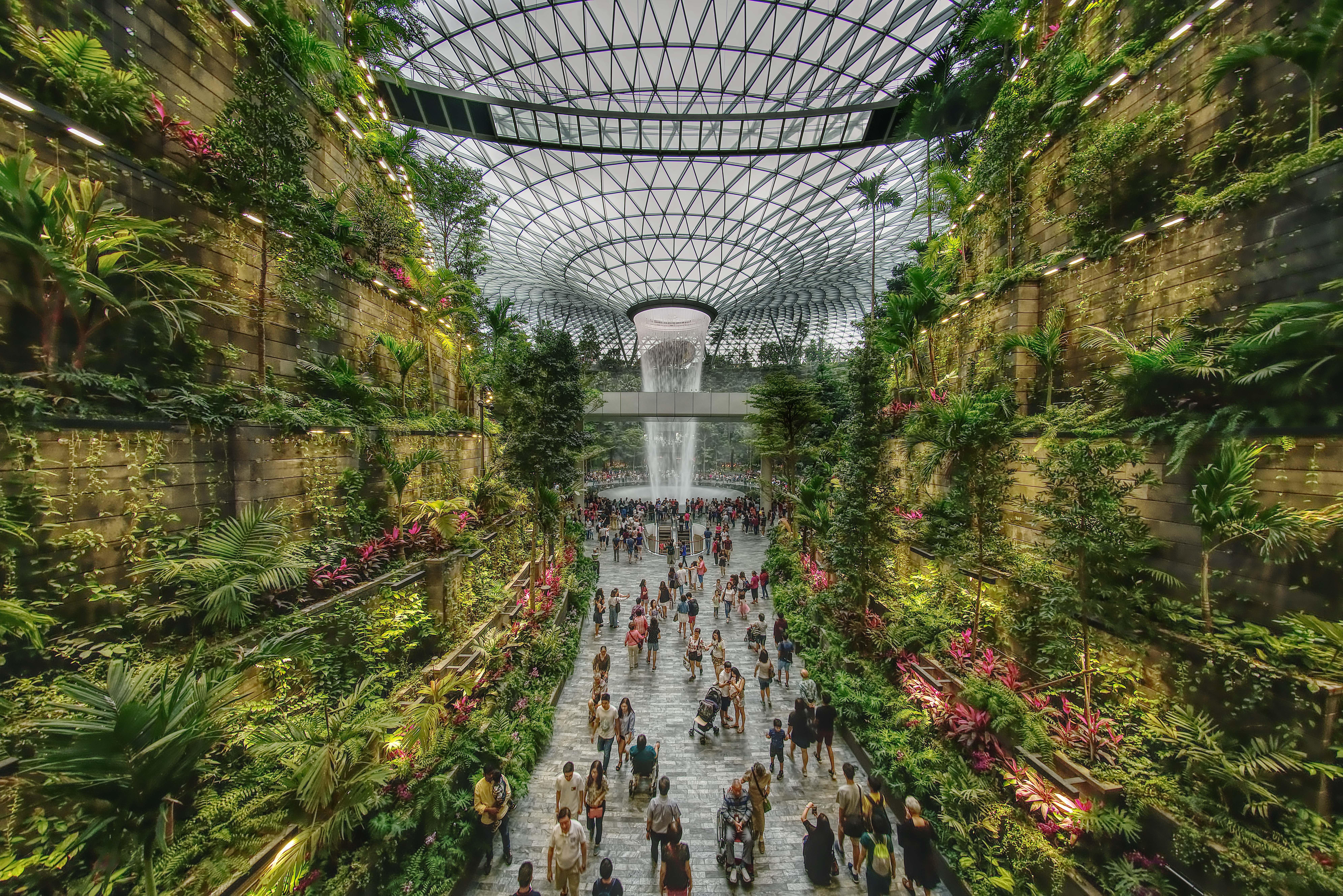 Crowne Plaza Changi Airport By Ihg Singapore Exterior foto The photo depicts a vibrant indoor garden space, characterized by lush greenery and a towering waterfall at its center. The setting features vertical gardens on stone walls, filled with various plants and flowers. People can be seen walking along the
