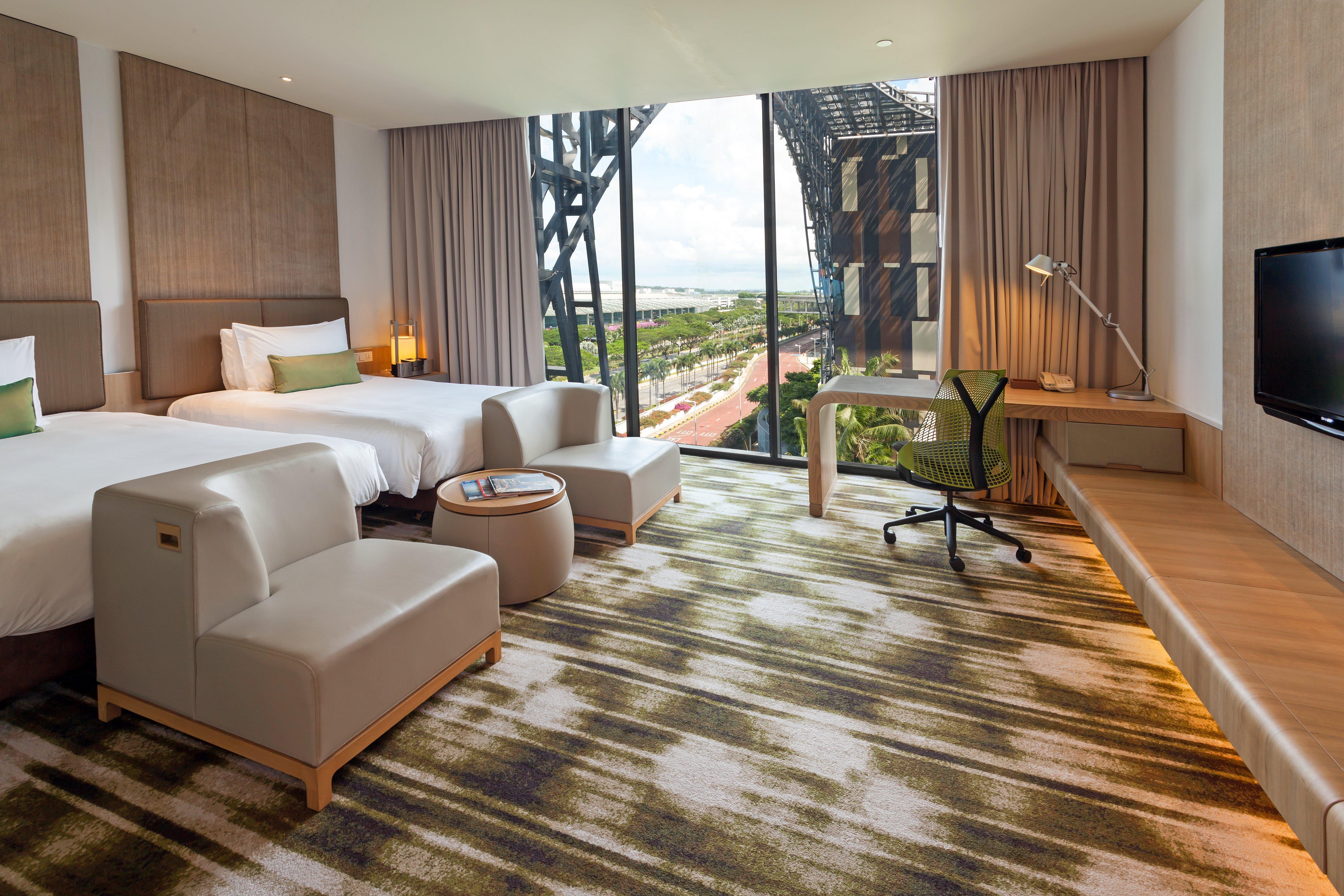 Crowne Plaza Changi Airport By Ihg Singapore Exterior foto The photo depicts a modern hotel room featuring two beds with white linens and a clean, minimalist design. There are two stylish armchairs and a small round table, creating a cozy seating area. The room includes a large window that offers a view of t