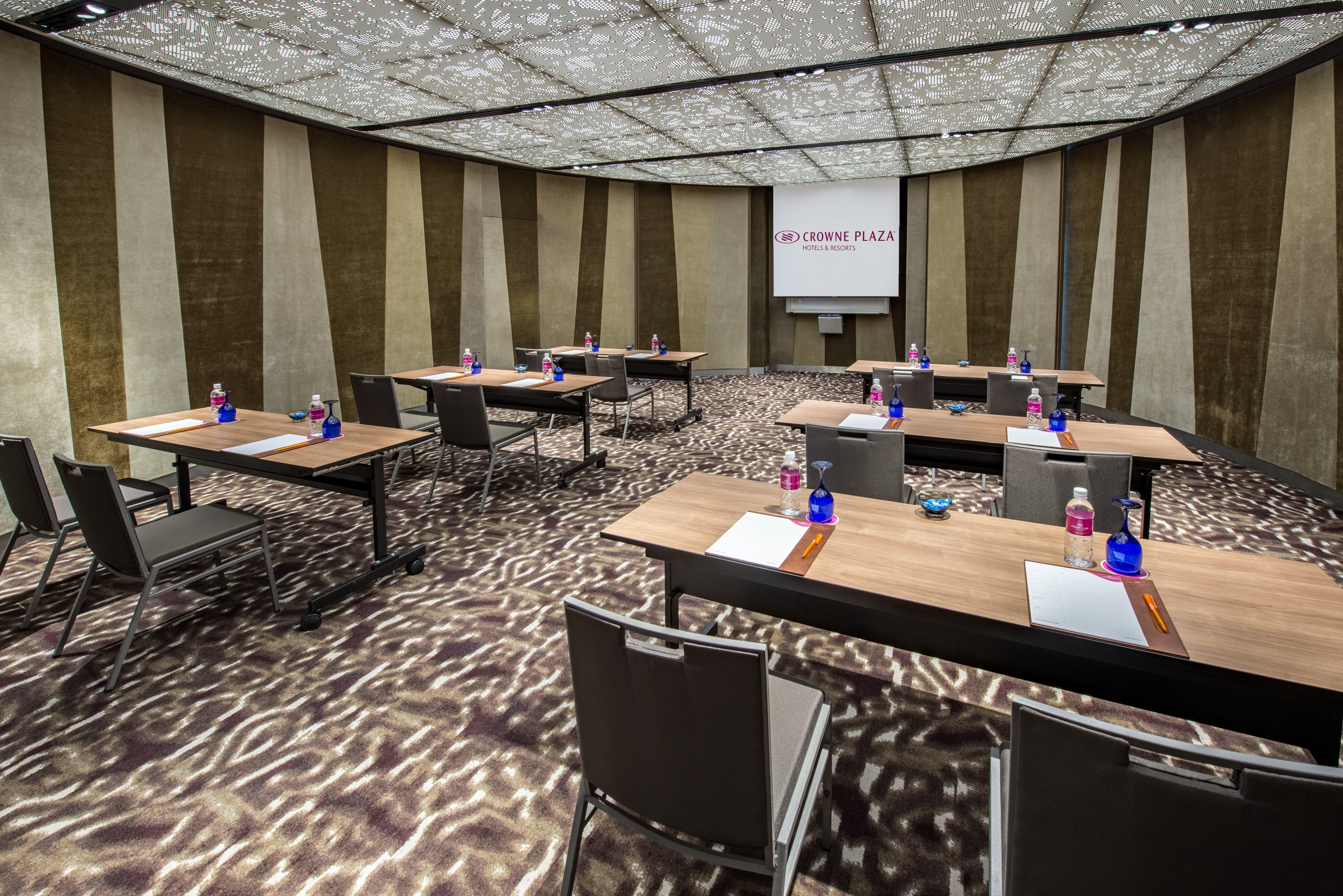 Crowne Plaza Changi Airport By Ihg Singapore Exterior foto The photo shows a modern conference room set up for a meeting or presentation. There are several wooden tables arranged in a U-shape, each equipped with a notepad and pen. Bottled water is placed in blue containers on the tables. The room features a 