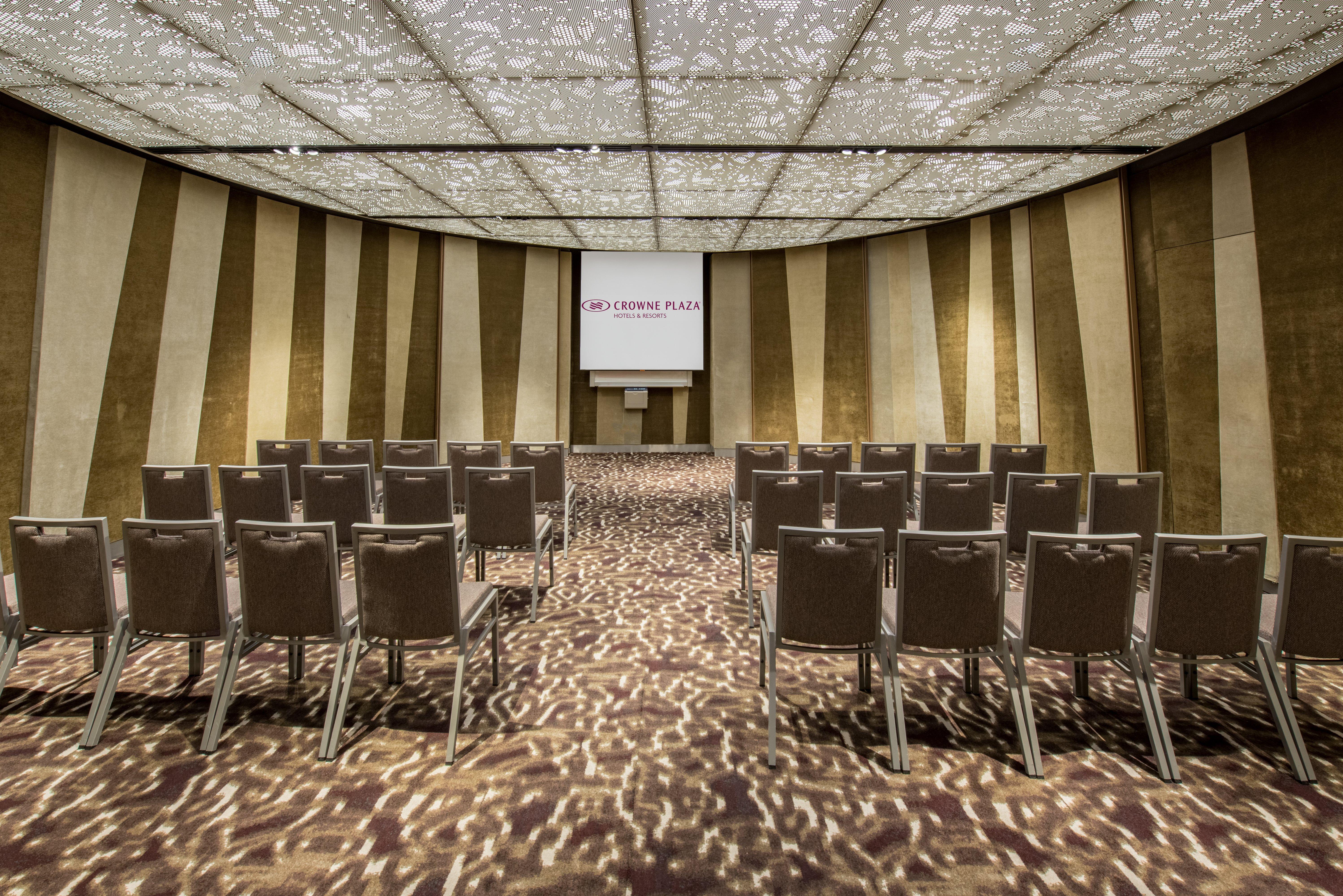 Crowne Plaza Changi Airport By Ihg Singapore Exterior foto The photo shows a conference or meeting room. It features rows of grey chairs arranged in a semi-circular layout, facing a screen at the front. The room has a decorative ceiling with a patterned design that allows light to filter through, creating in