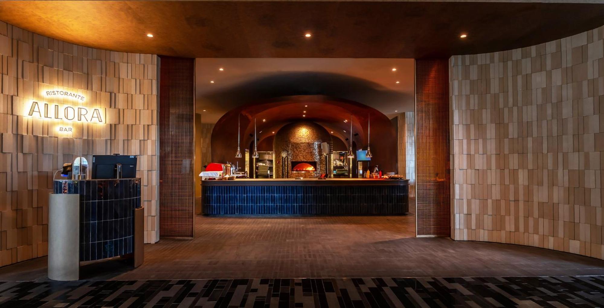 Crowne Plaza Changi Airport By Ihg Singapore Exterior foto The photo shows an interior space that appears to be a restaurant or dining area. In the background, there is a long counter, likely serving food, with an arched design above it. The counter is lined with various food items, possibly in warming trays