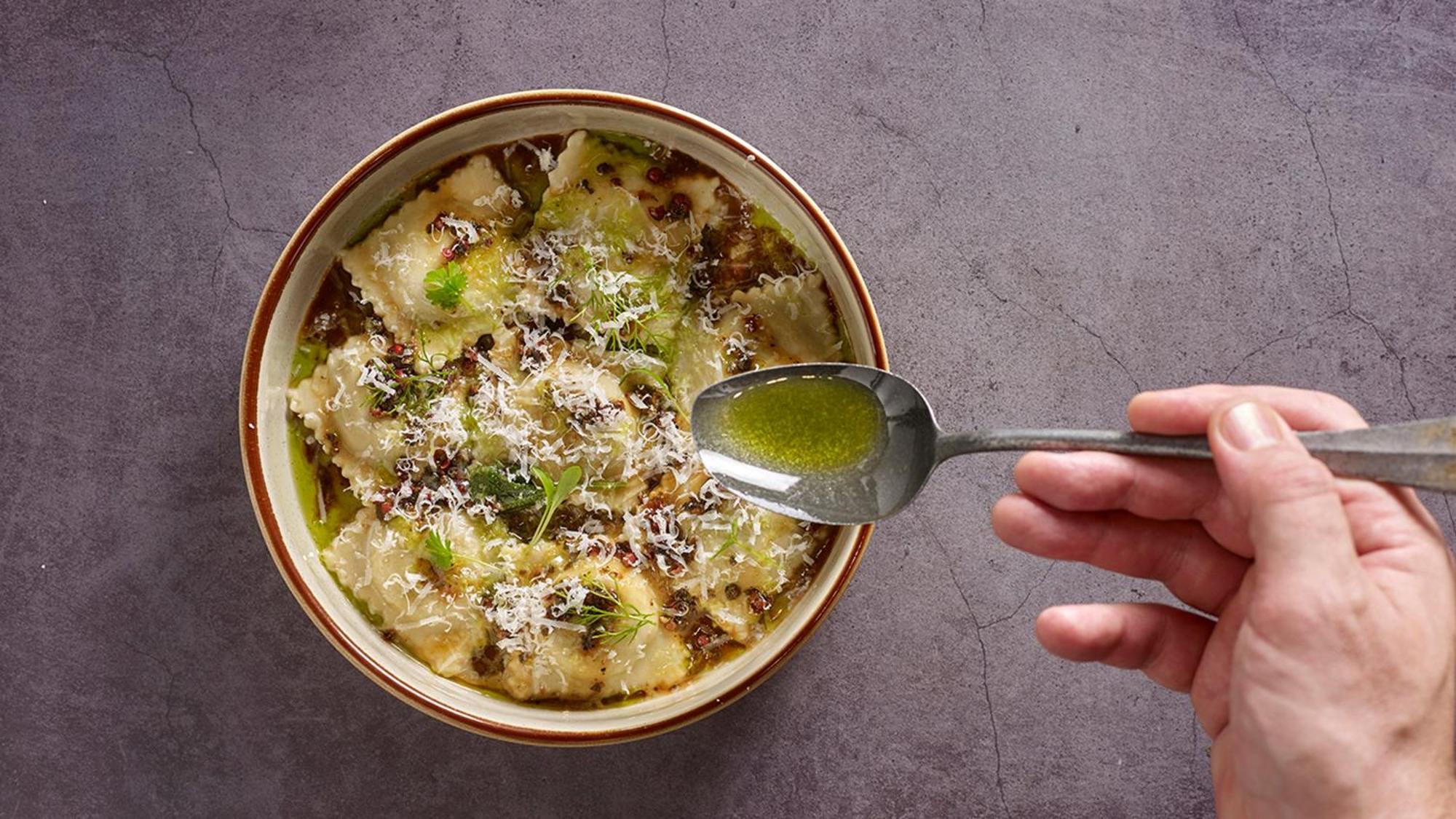 Crowne Plaza Changi Airport By Ihg Singapore Exterior foto The photo shows a bowl of ravioli garnished with grated cheese and drizzled with olive oil. A hand is holding a spoon above the bowl, indicating the action of adding more oil or sauce. The dish appears delicious and is presented with an appealing aes
