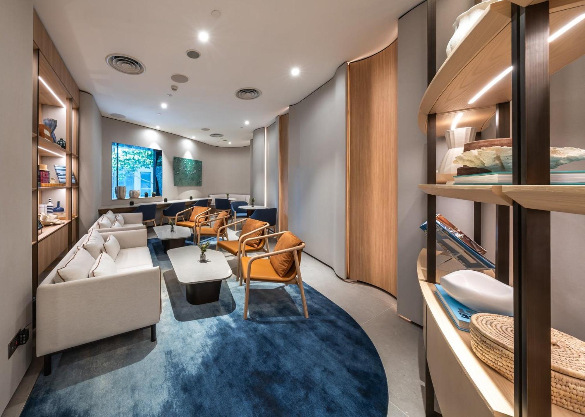 Crowne Plaza Changi Airport By Ihg Singapore Exterior foto The photo shows a modern and elegantly designed waiting area or lounge. It features soft, neutral-colored furniture, including white sofas and stylish orange chairs. The space has a warm ambiance with ambient lighting and wooden accents. A blue circu