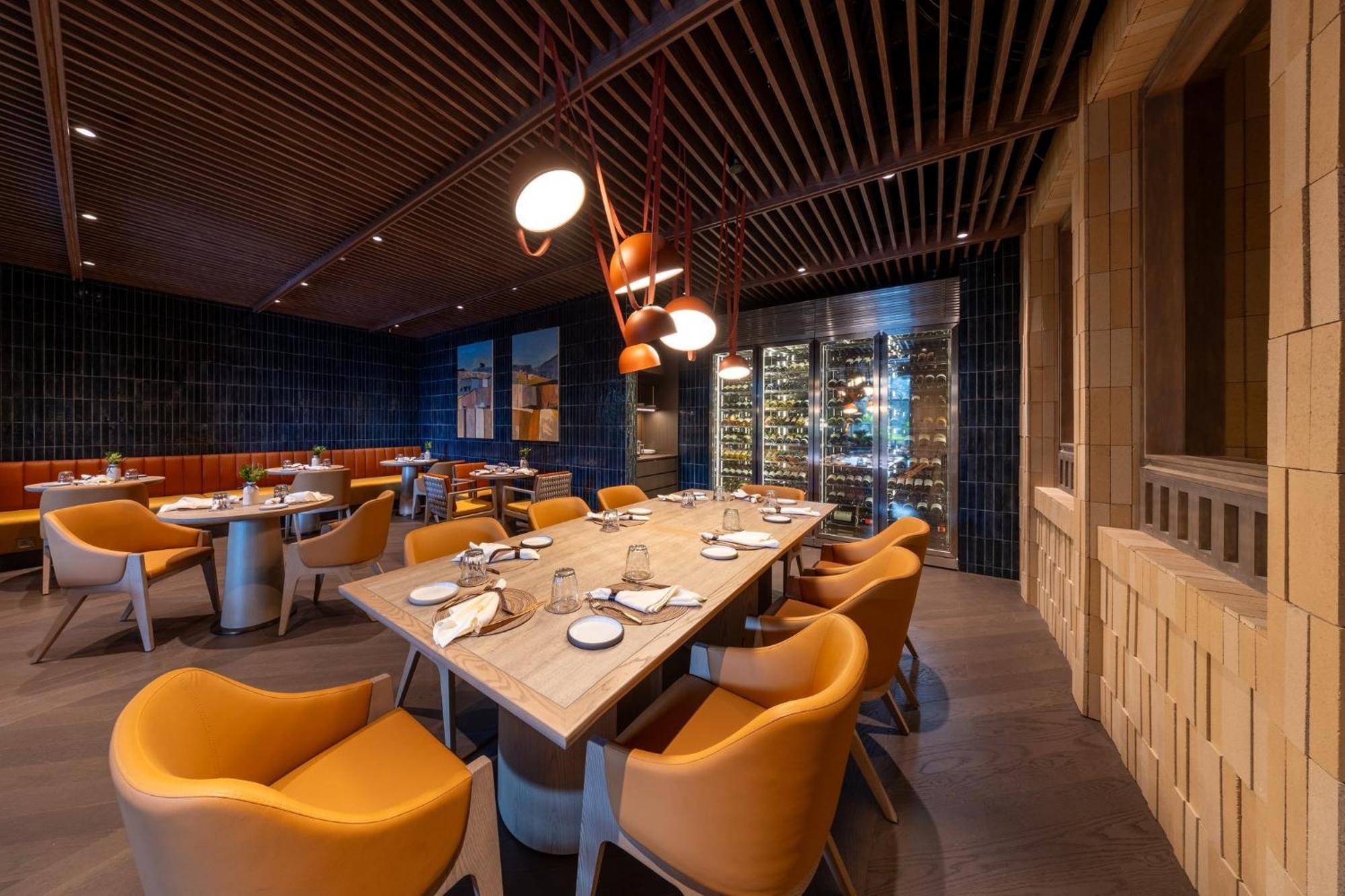 Crowne Plaza Changi Airport By Ihg Singapore Exterior foto The photo shows an elegant restaurant interior featuring a modern design. In the center, there is a large wooden table set for dining, with white plates and utensils arranged neatly. Surrounding the table are vibrant orange chairs that provide a cozy