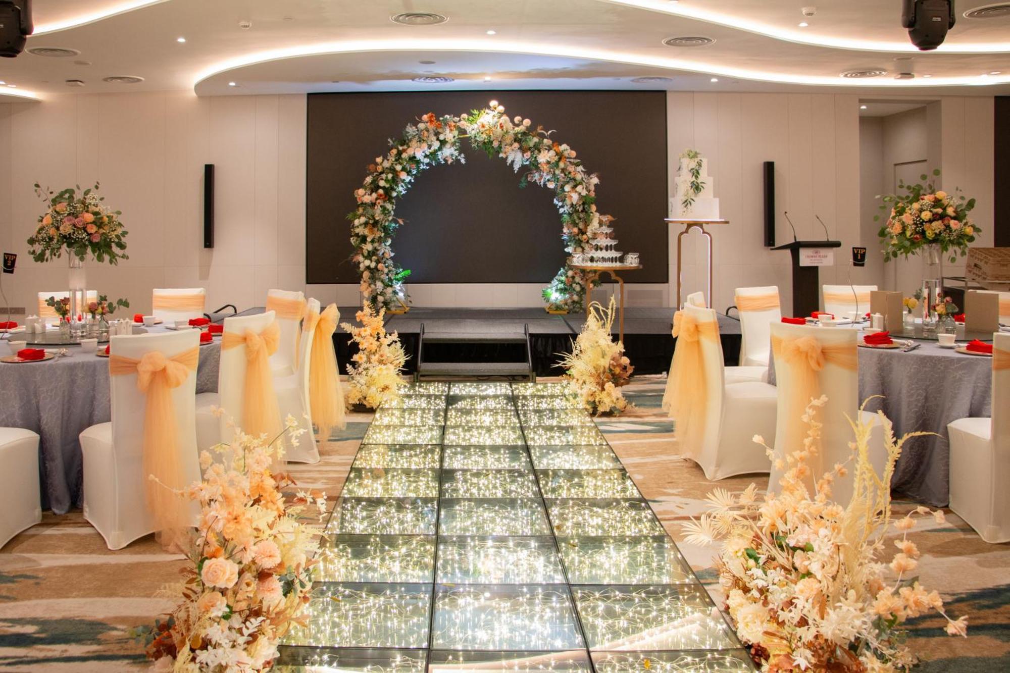 Crowne Plaza Changi Airport By Ihg Singapore Exterior foto The image depicts an elegantly decorated event space, likely for a wedding or formal occasion. In the center, there is a flower-adorned archway in warm colors, creating a focal point. A sparkling, illuminated pathway leads towards the arch, bordered 