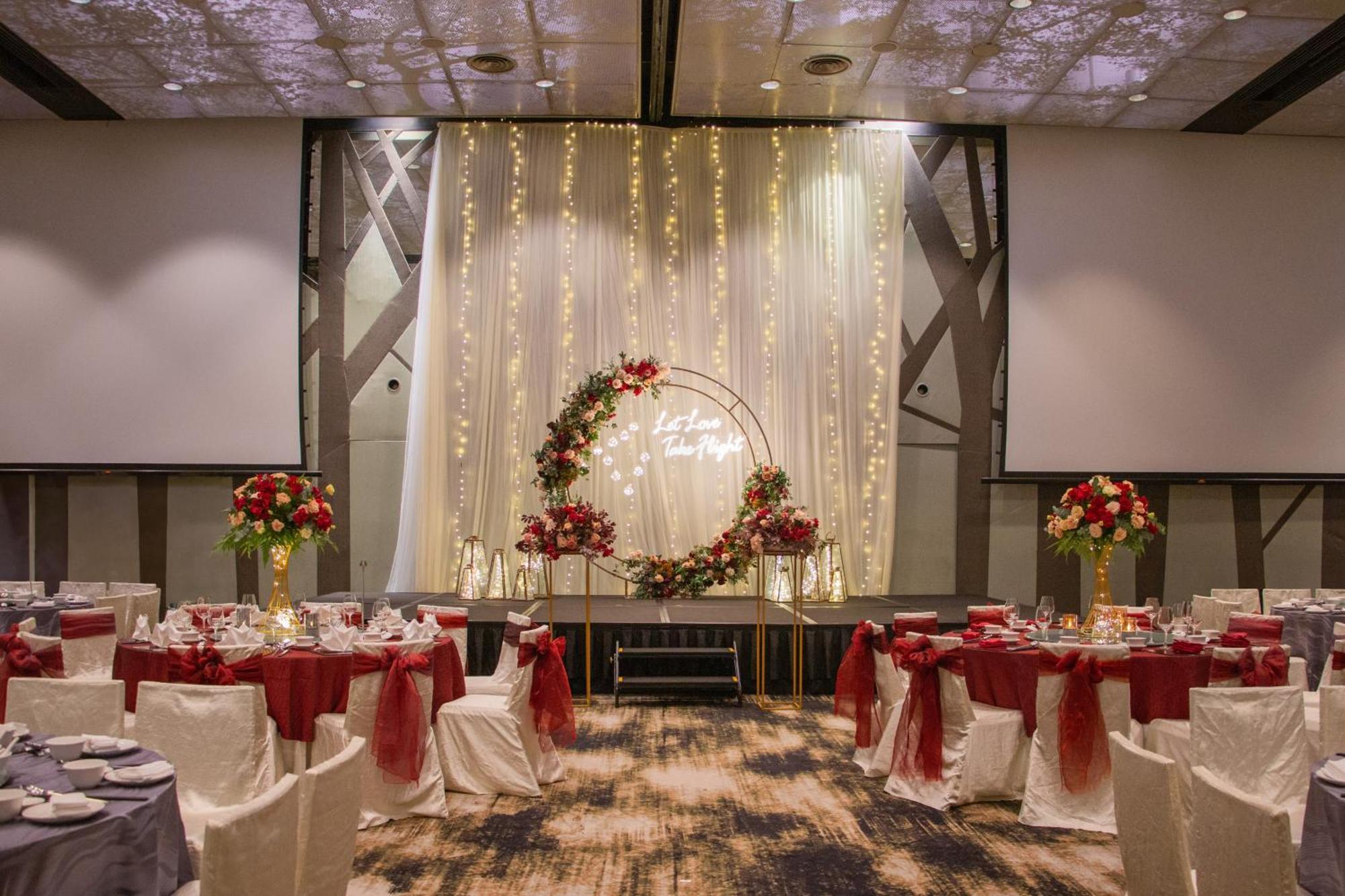 Crowne Plaza Changi Airport By Ihg Singapore Exterior foto The photo shows an elegantly decorated banquet hall set up for an event. There are round tables with white tablecloths, each adorned with a red centerpiece. The chairs have white covers and are draped with red sashes. At the back of the room, there i