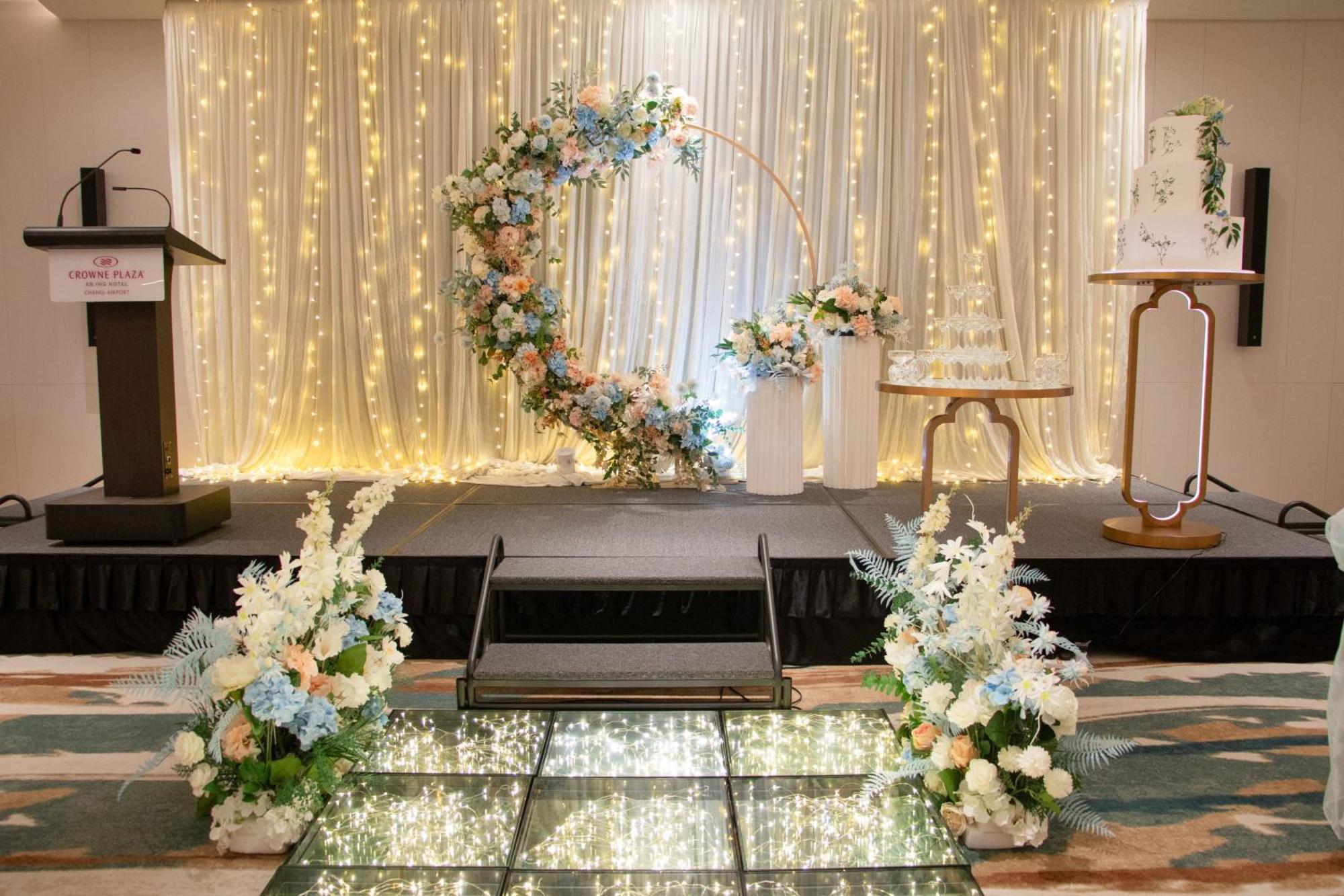 Crowne Plaza Changi Airport By Ihg Singapore Exterior foto The photo shows a beautifully decorated event space, likely for a wedding or special occasion. In the background, there is a shimmering curtain with fairy lights that create a warm, romantic ambiance. 

At the center, there is a circular floral arch 