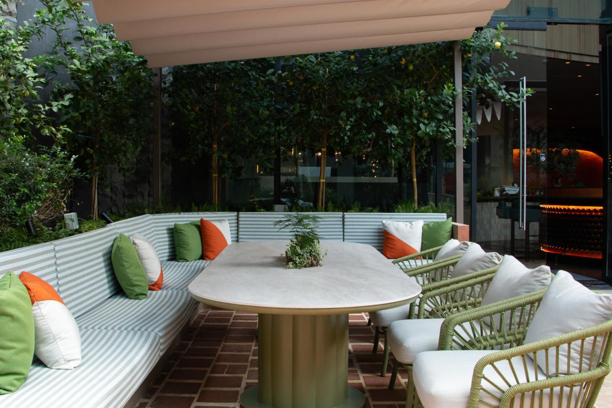 Crowne Plaza Changi Airport By Ihg Singapore Exterior foto The photo shows a stylish outdoor seating area. There is a large, oval table at the center, surrounded by comfortable chairs with white cushions. The seating features a long, curved bench with a light green and white striped design, and it is adorned