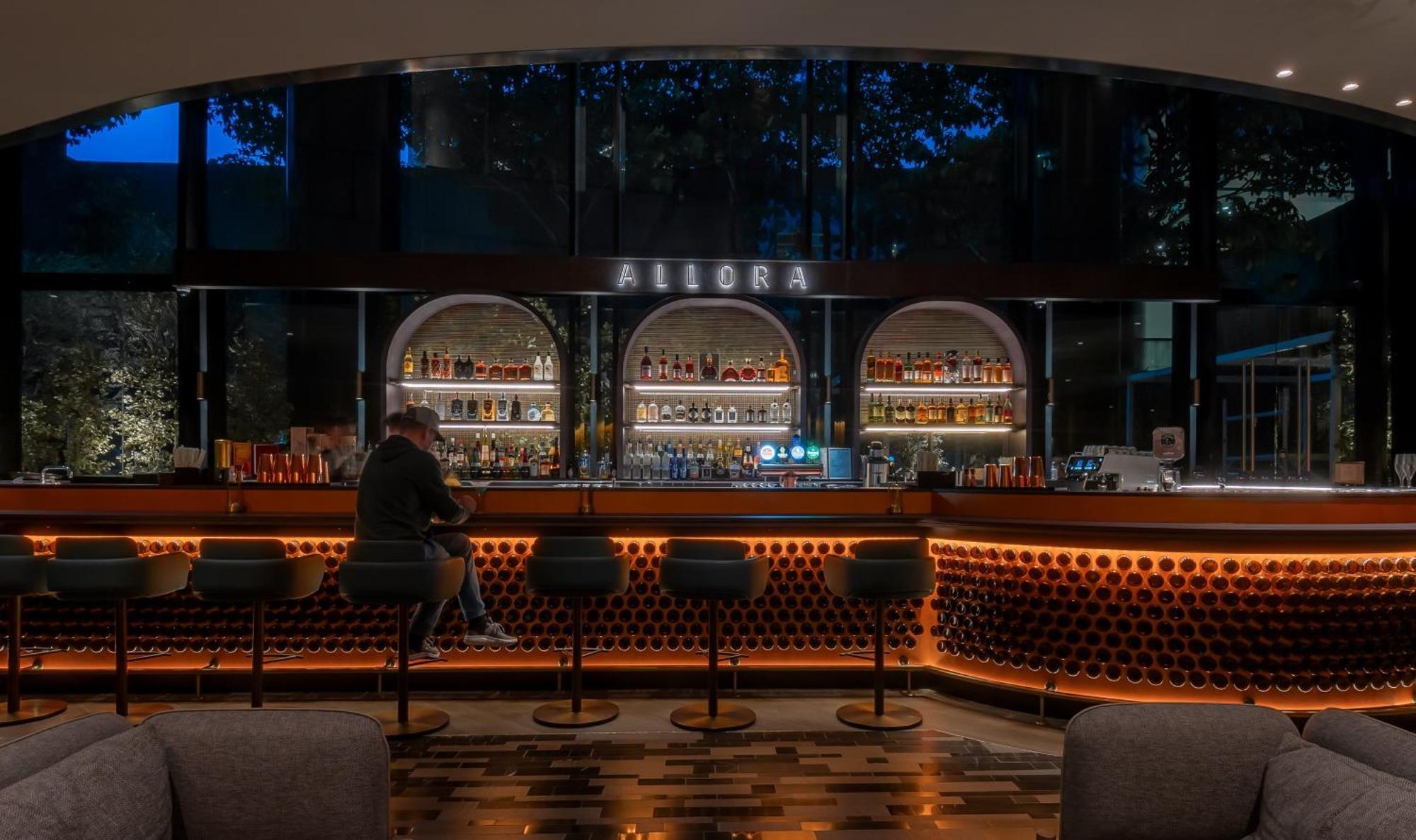 Crowne Plaza Changi Airport By Ihg Singapore Exterior foto The photo shows a bar area with a modern and stylish design. In the center, there is a well-lit bar counter featuring a variety of alcoholic beverages displayed on shelves behind it. The bar has a sleek, contemporary look with circular light fixtures
