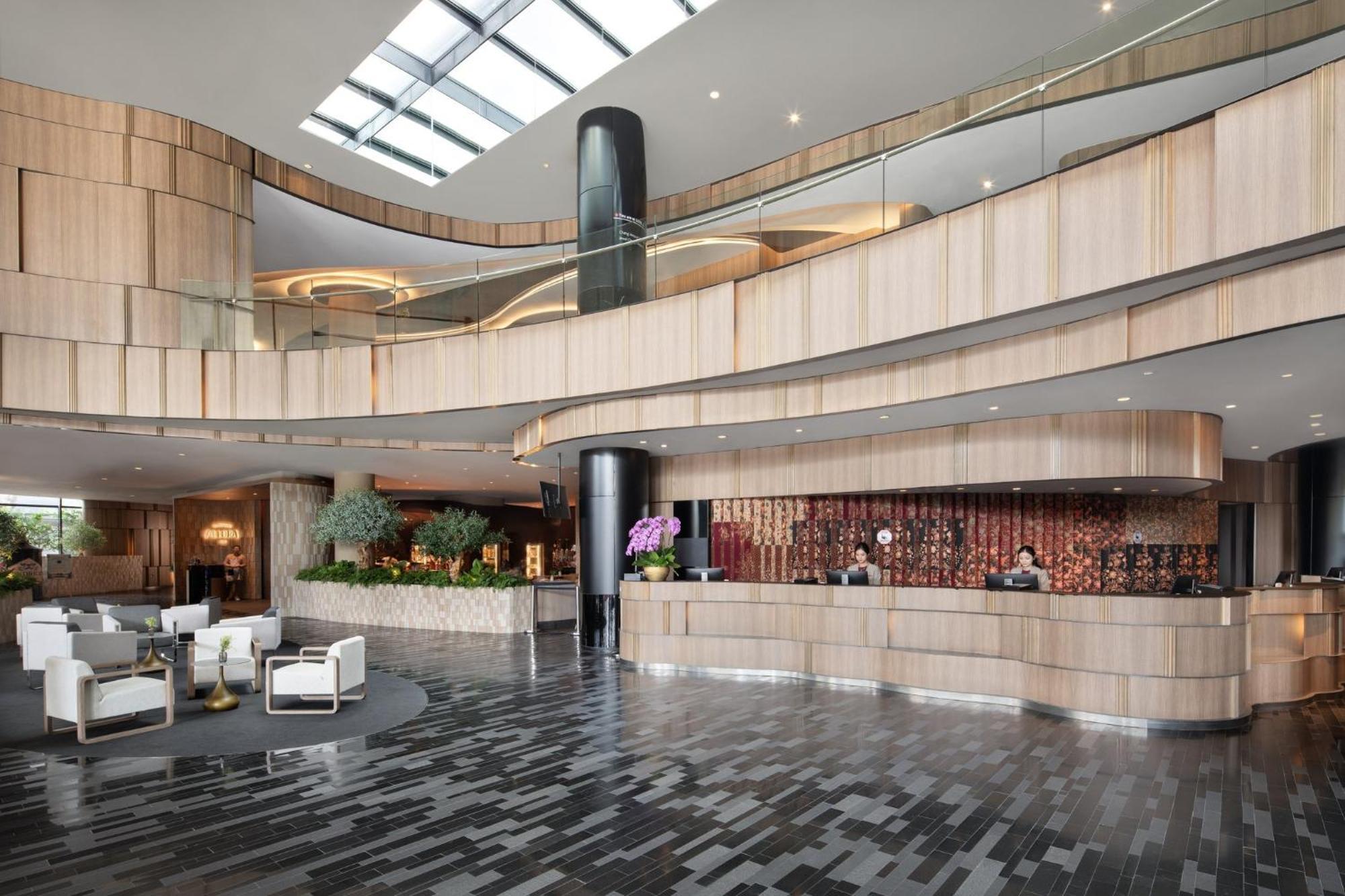 Crowne Plaza Changi Airport By Ihg Singapore Exterior foto The photo shows a modern hotel lobby with a sleek and stylish design. The reception area features a curved wooden counter, with staff members attending to guests. The interior design includes a mix of wood and stone materials, creating a warm and inv